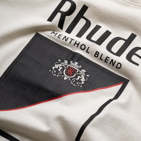 Close-up view of Rhude Collins Fumar Tee showing embroidered crest and tobacco-inspired graphic